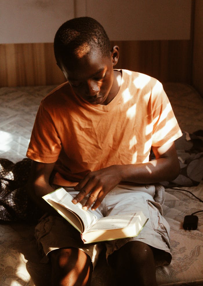 class-04 A young boy reading a book in a sunlit room with light and shadow play.